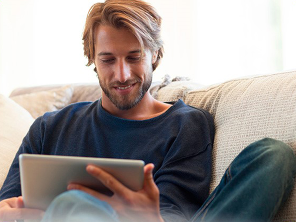Mann sitzt lässig auf dem Sofa mit Tablett in der Hand und liest