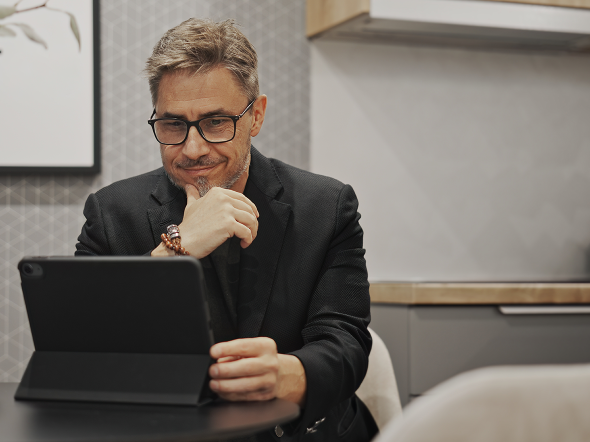 Mann sitzt am Tisch und schaut auf ein Tablet